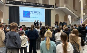Jugendliche stehen in einer Halle vor einer Bühne mit Leinwand. Darauf steht „Roberta Challenge Hannover".