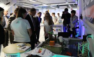 Gruppe von Personen betrachtet ein Robotik-Modell auf einem Tisch mit "Roberta"-Schild; Kamerateam im Hintergrund.
