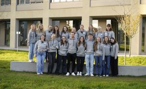 Gruppe von ca. 20 Personen in grauen Hoodies posiert lächelnd vor einem modernen Gebäude auf einer Rasenfläche.